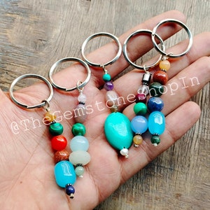 May include: Four silver keyrings with colourful gemstone beads. Each keyring features a different combination of beads, including turquoise, lapis lazuli, amethyst, and rose quartz. The keyrings are perfect for adding a touch of colour and personality to your keys.
