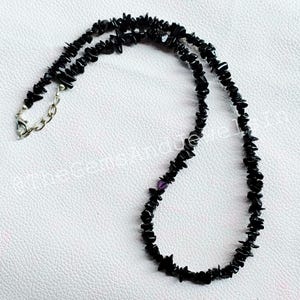 May include: A black gemstone necklace with a silver clasp and chain. The necklace is made of small, irregularly shaped black stones. A small purple stone is also visible in the necklace.