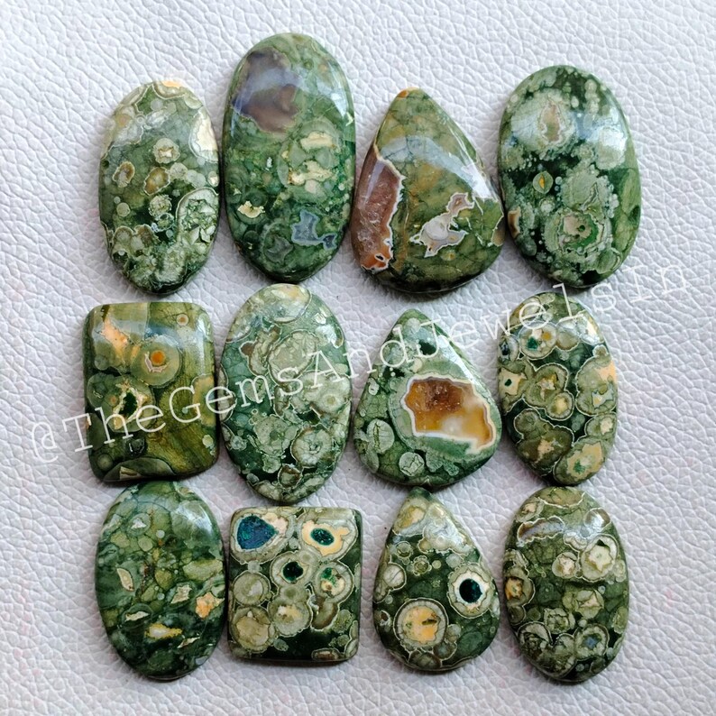 May include: A collection of 12 green, brown, and white ocean jasper cabochons. The cabochons are various shapes and sizes, with a speckled pattern.