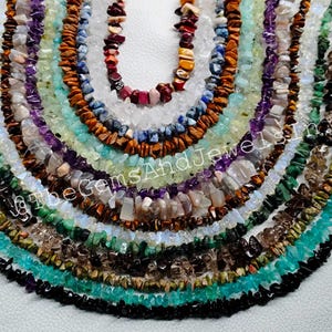 May include: A selection of gemstone chip necklaces in a range of colours, including purple, green, brown, and blue. The necklaces are arranged in a circular pattern, displaying the diverse hues and textures of the natural stones. The image is well-lit, highlighting the details of each chip.