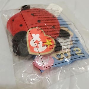 Può includere: Un giocattolo di peluche Beanie Baby a forma di coccinella rossa e nera nella sua confezione originale. La confezione è blu e bianca con il logo Ty e le parole "McDonald's Corporation" e "Stampato in Cina".