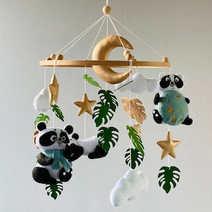 May include: A baby mobile with a wooden ring, a crescent moon, two panda bears, two stars, three clouds, and green leaves. The mobile is made of felt and fabric.