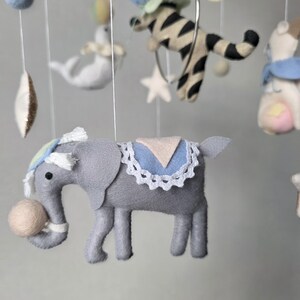 May include: A handmade baby mobile featuring felt circus animals. The mobile includes a gray elephant with a ball, a zebra in a hoop, a white seal, and other colorful felt shapes. The mobile is suspended from a wooden hoop.