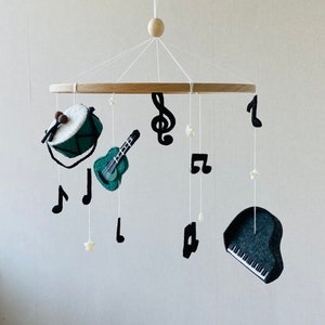 Op de afbeelding: Een zwart-witte muzikale mobiel met een drum, gitaar, piano en solsleutel. De mobiel is gemaakt van vilt en hangt aan een houten ring.