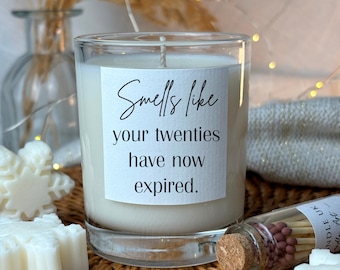 May include: A white candle in a glass jar with a label that reads "Smells like your twenties have now expired."