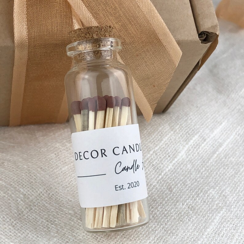 May include: A glass jar filled with wooden matches with brown tips. The jar has a white label with the text "DECOR CANDLE Candle Co. Est. 2020".
