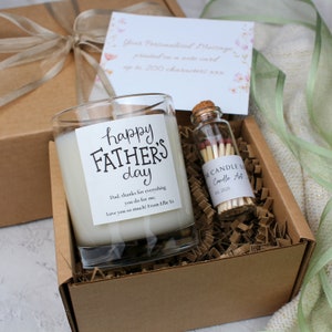 May include: A brown cardboard gift box with a clear glass candle inside. The candle has a white label with the text "happy FATHER'S day" and a personalized message. The box also contains a small glass bottle with matches.