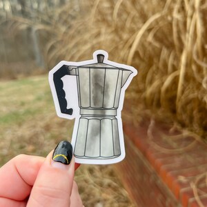May include: A silver and black metal coffee maker sticker. The sticker is on a white background.