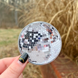 May include: A silver disco ball sticker with a mirrored surface. The sticker is round and has a diameter of approximately 3 inches.