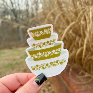 May include: A stack of three vintage-style mixing bowls with a white background and a green floral pattern. The bowls are nested inside each other.