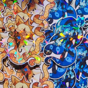 Pode incluir: Uma coleção de autocolantes holográficos com dois designs distintos. Um design apresenta uma personagem com um adorno floral e um corpo semelhante a uma serpente em tons de ouro e laranja. O outro design apresenta uma criatura azul com uma forma semelhante.