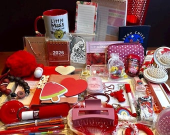 May include: A collection of red and pink items, including a mug, pens, hair accessories, and a tumbler, arranged on a wooden tray. Other items include a calendar, a polka-dot cosmetic bag, and a small notebook. The items are arranged on a wooden surface.