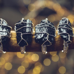 Könnte beinhalten: Vier Ringe mit rohen, schwarzen Turmalinkristallen, die mit silberfarbenem Draht umwickelt sind. Jeder Ring zeigt einen einzigartigen, gezackten Stein mit metallischem Glanz, der von einem strukturierten Drahtband an der Basis gehalten wird.