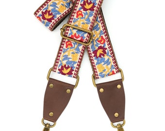 May include: A brown leather camera strap with gold-tone hardware and a colorful floral patterned fabric strap.