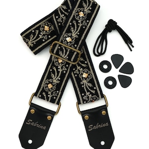May include: Black guitar strap with gold floral embroidery and the name "Sabrina" printed on the leather ends. Includes a black cord, two black strap locks, and three black guitar picks. The strap has a gold-coloured metal buckle.