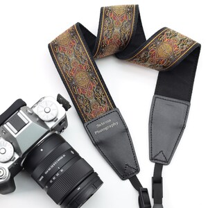 May include: A black camera strap with a colorful patterned fabric strap and a leather patch that says "Sabrina Photography".