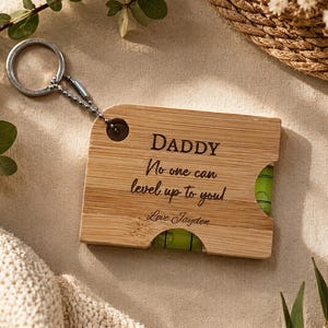 May include: A wooden keychain with a level, featuring the text "DADDY No one can level up to you! Love Jayden." The keychain has a silver ring and chain, and a green bubble level.