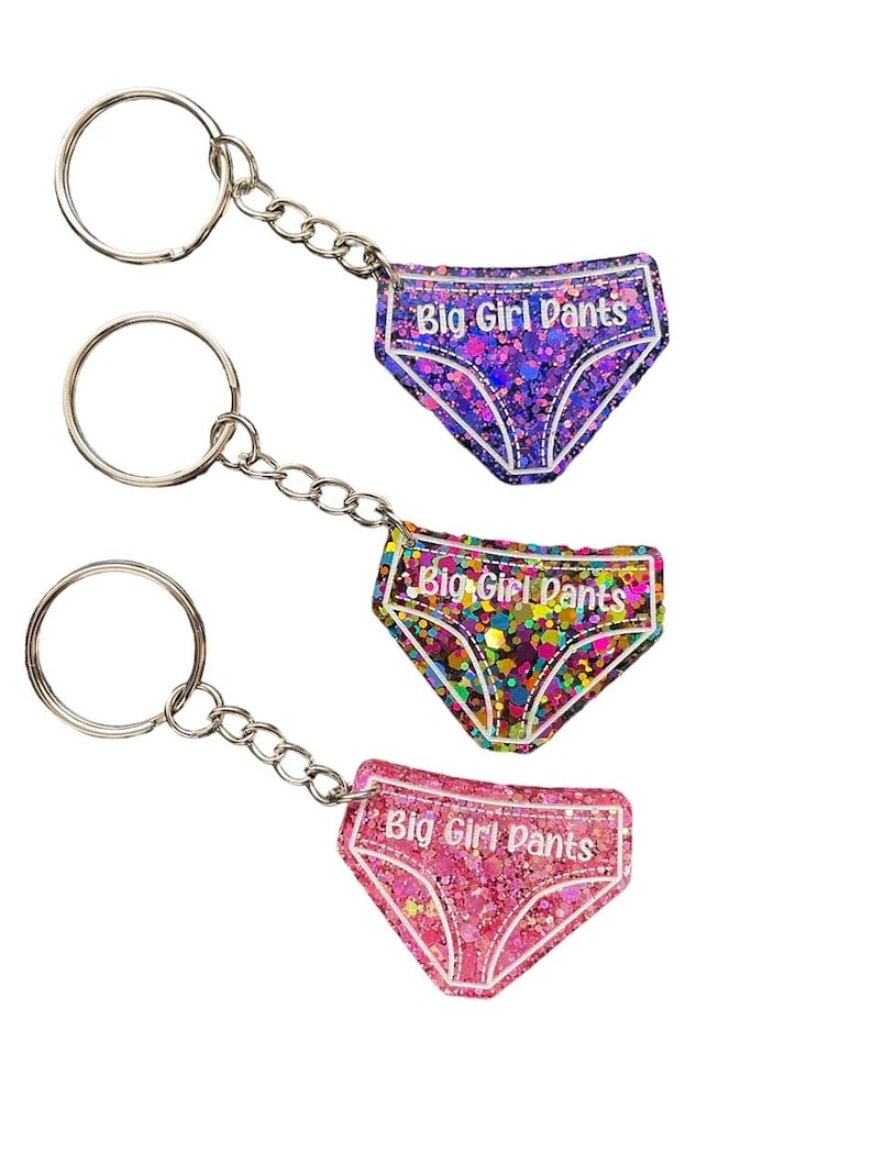 Peut inclure: Trois porte-cl&eacute;s avec des breloques en r&eacute;sine remplies de paillettes en forme de sous-v&ecirc;tements. Chaque breloque porte l'inscription "Big Girl Pants". Les breloques sont violettes, multicolores et roses.