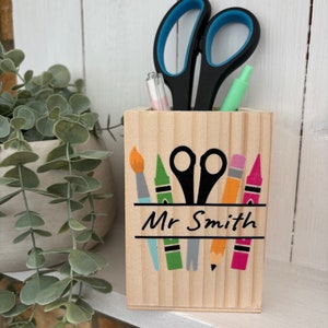 May include: Wooden pencil holder with a painted design of crayons, a paintbrush, scissors, and a pencil. The holder is personalised with the name "Mr. Smith".