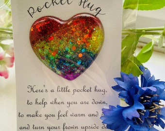 May include: A white card with the text "Pocket Hug" and a rainbow glitter heart attached. The card reads "Here's a little pocket hug, to help when you are down, to make you feel warm and and turn your frown upside d"