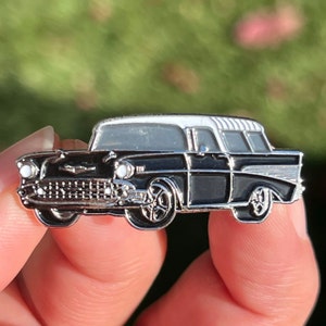 May include: Black and white enamel pin of a 1957 Chevrolet Nomad station wagon.