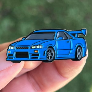 May include: A blue enamel pin of a Nissan Skyline R34, a popular Japanese sports car.