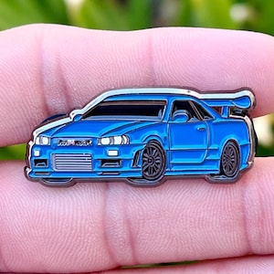 May include: A blue enamel pin of a Nissan Skyline R34, a popular Japanese sports car.