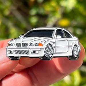 Peut inclure: Une épingle en émail blanc représentant une BMW M3 E46. L'épingle est détaillée avec des contours noirs et une calandre argentée.