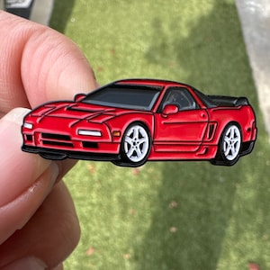 Puede incluir: Un pin de esmalte rojo de un coche deportivo Honda NSX. El coche tiene detalles en negro y ruedas blancas.