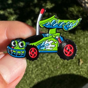 Puede incluir: Un coche de juguete verde y azul con una antena negra y ojos grandes. El coche tiene un diseño de llama blanca y ruedas negras con detalles rojos.