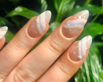 Puede incluir: Primer plano de una mano con uñas de color carne con un diseño de arcoíris y estrellas blancas.
