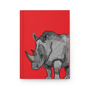 May include: A hardcover journal featuring a vibrant red background and a stylized illustration of a rhinoceros. The rhinoceros is rendered in shades of grey and white with intricate black line work creating a textured, geometric appearance.