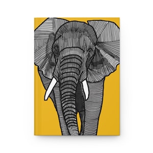 May include: A rectangular notebook featuring a graphic illustration of an elephant head on a solid yellow background. The elephant is rendered in black and white with detailed line work and shading, showcasing large ears and two white tusks.