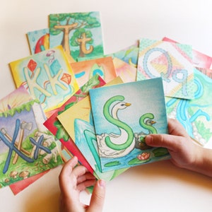May include: A set of colorful alphabet cards featuring hand-painted illustrations of letters and scenes. The cards are made of thick paper and are perfect for learning the alphabet.