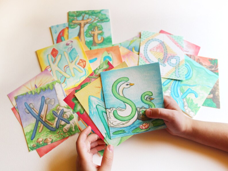 May include: A set of colorful alphabet cards featuring hand-painted illustrations of letters and scenes. The cards are made of thick paper and are perfect for learning the alphabet.