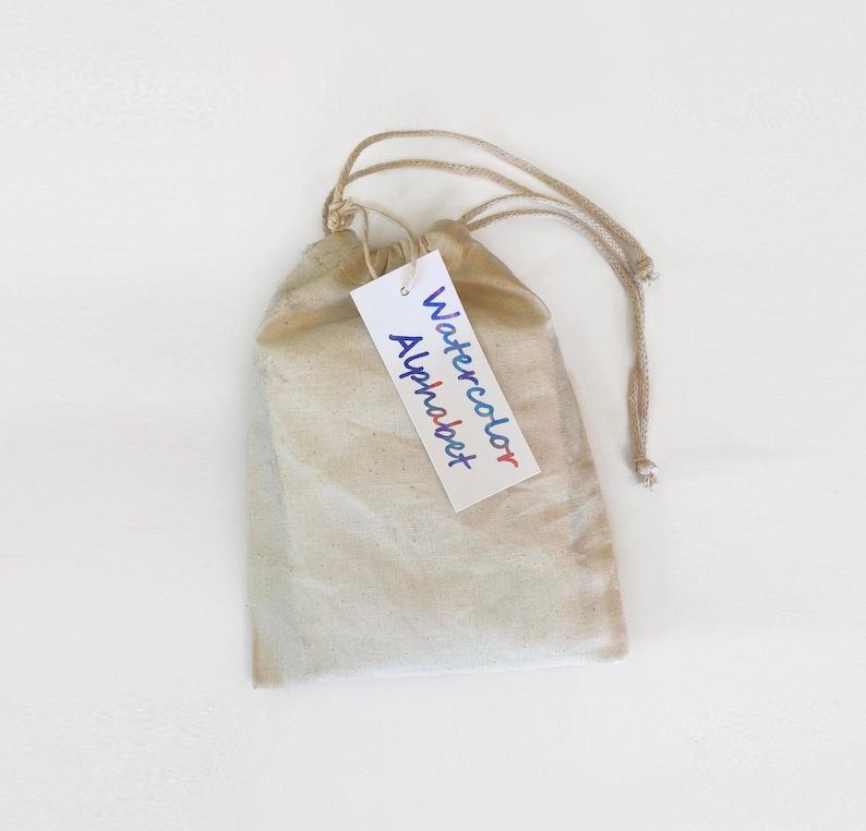 May include: A white drawstring bag with a tag that says "Watercolor Alphabet".