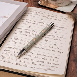 May include: A close-up of a pen with a green and white butterfly design on a notebook with handwritten text. The text reads "The flapping of its wings Similar to a fly. But when listening carefully you can hear the droning reply. Once heard you immediately Yellow flowers black flowers to Surplus. Buzzing flower to flower the Shy. People may there is more than aimlessly through. reluctant to admit. It holds the poll ose to its chest like a baby. Its pri passion, life-even more maybe a time when life must end Silence. But before this it Cannot comprehend. Sting, buzzi must go through what we Organs torn, it carries on - Flower to flower. Weaher and weaker. Dead before long. The yellow for"