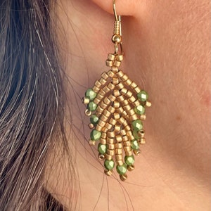 May include: Gold and green beaded dangle earrings. The earrings are made with small gold beads and green glass beads. The earrings are hanging from a gold hook.