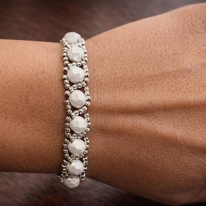 May include: A beaded bracelet featuring white, faceted beads and silver-colored spacers. The bracelet is worn on a wrist, showcasing the jewelry's design and texture. The bracelet's design is symmetrical, with the white beads evenly spaced.
