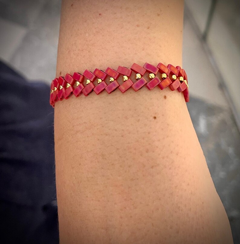 May include: A pink and gold beaded bracelet with a geometric pattern.