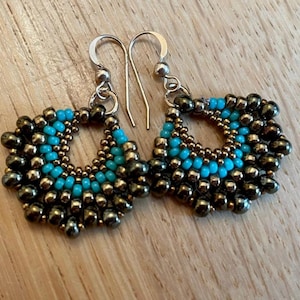 May include: A pair of dangle earrings with a silver hook and a beaded design. The beads are in shades of brown and turquoise.