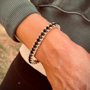 Könnte beinhalten: Ein schwarzes und weißes Perlenarmband mit elastischem Design. Das Armband besteht aus kleinen, runden Perlen, die sich in der Farbe abwechseln.
