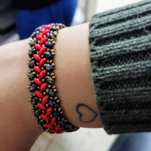 May include: A red and black beaded bracelet with a chevron pattern. The bracelet is worn on a person's wrist.