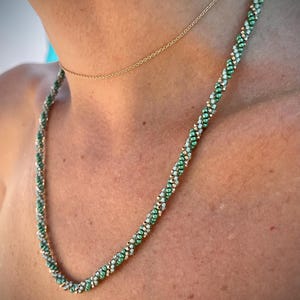 May include: A green and white beaded necklace with a gold chain necklace layered on top.