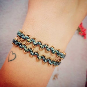 Puede incluir: Un brazalete de cuentas con un patrón en zigzag en tonos azules y dorados.