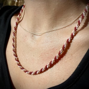 May include: A red and pink beaded necklace with a twisted design. The necklace is layered over a thin silver chain.