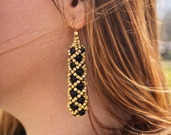 May include: Gold-toned beaded earrings with a cylindrical design. The earrings feature alternating rows of black beads and gold-colored beads, creating a textured pattern. The earrings are suspended from a gold-colored hoop.