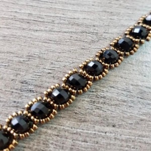 May include: A black beaded bracelet with gold accents. The bracelet is made with small, round beads and is strung on a thin, gold chain.