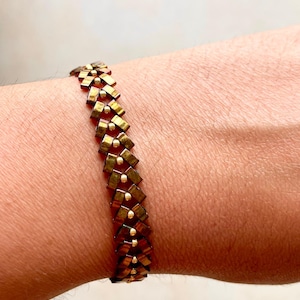 May include: A gold and brown beaded bracelet with a geometric pattern.