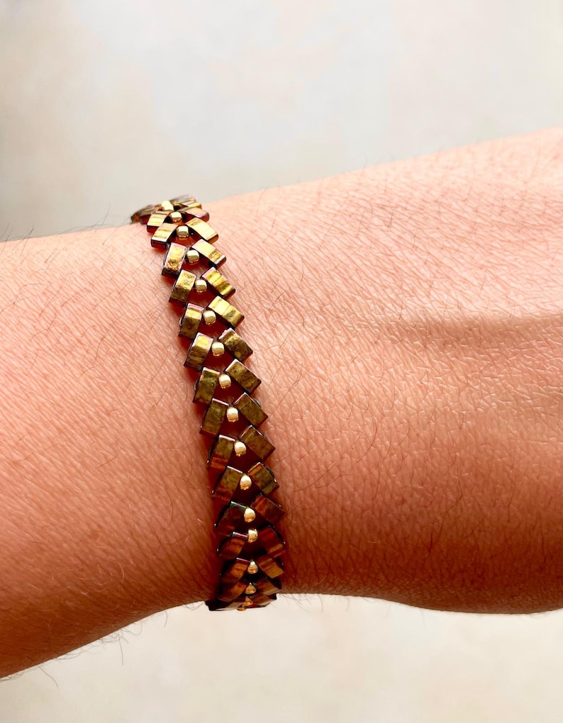 May include: A gold and brown beaded bracelet with a geometric pattern.